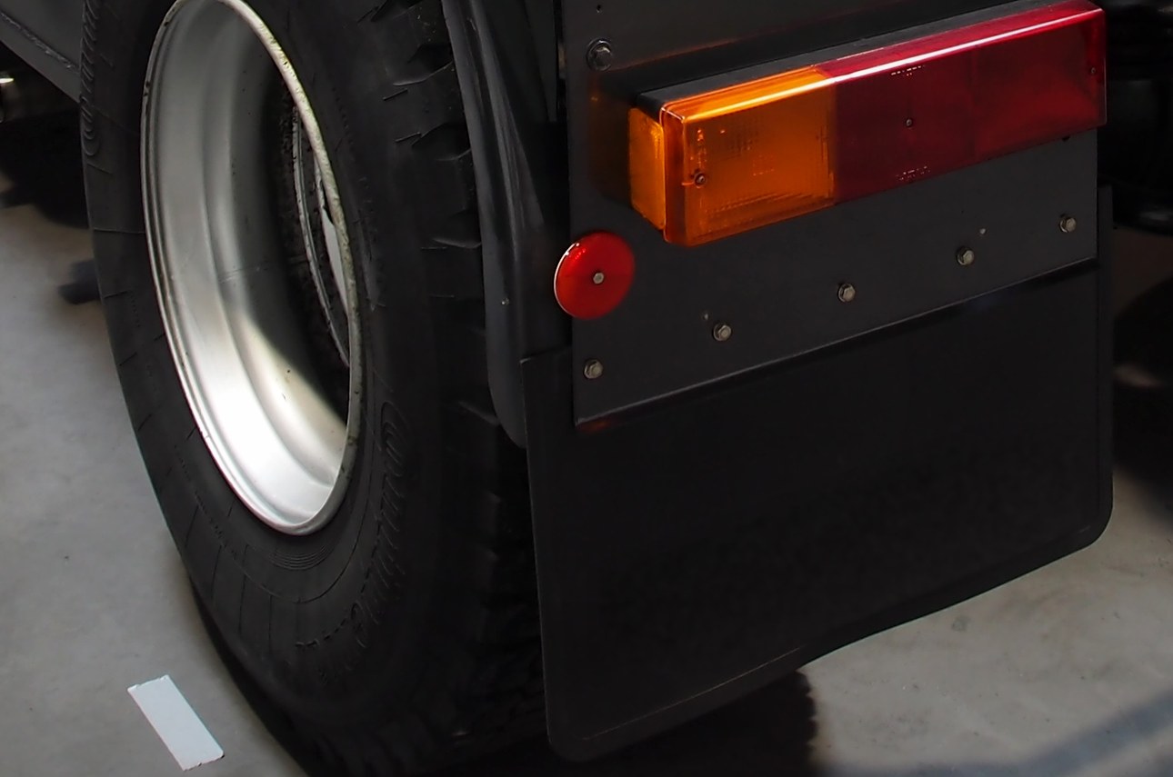 Plain black rubber mud flap and tail light on the rear of a tractor (illustrative photo)